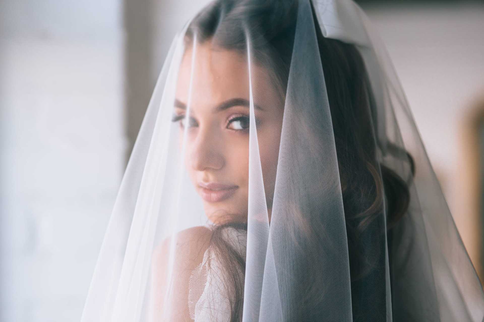 Bride with soft curls wearing a sheer veil, gazing back over her shoulder.