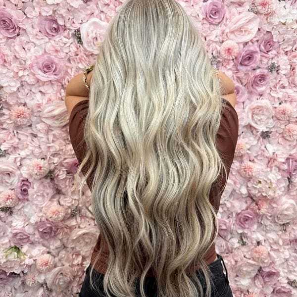 Long, wavy blonde hair against a pink floral wall backdrop.