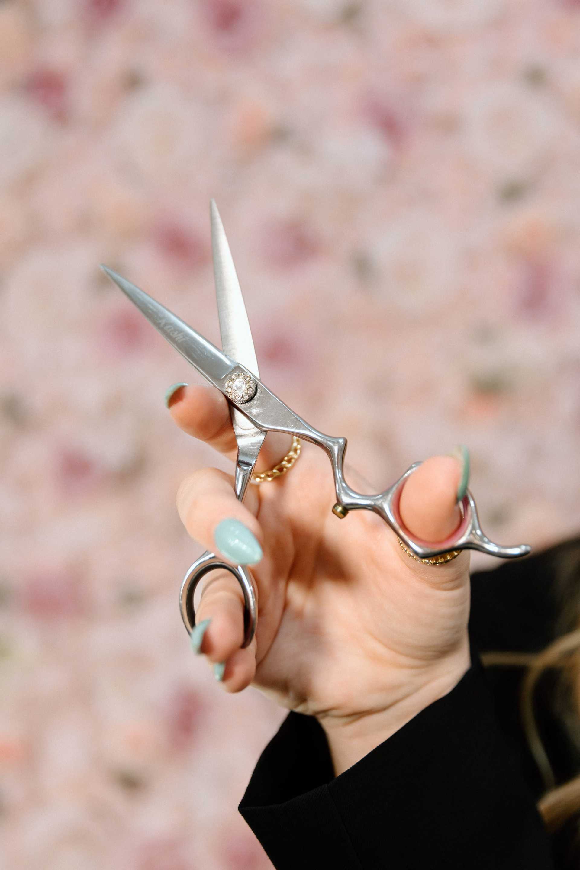 Hand holding professional hair scissors against floral background.