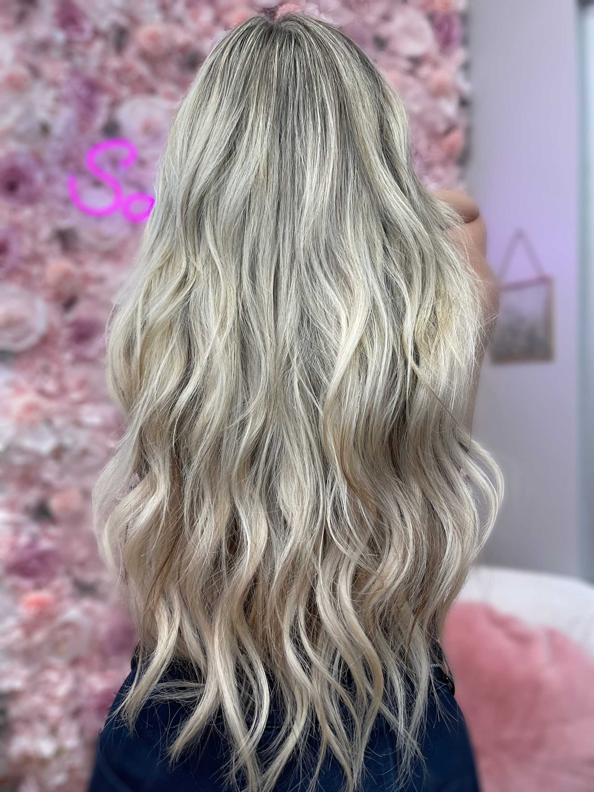 Long, wavy blonde hair against a floral pink backdrop.