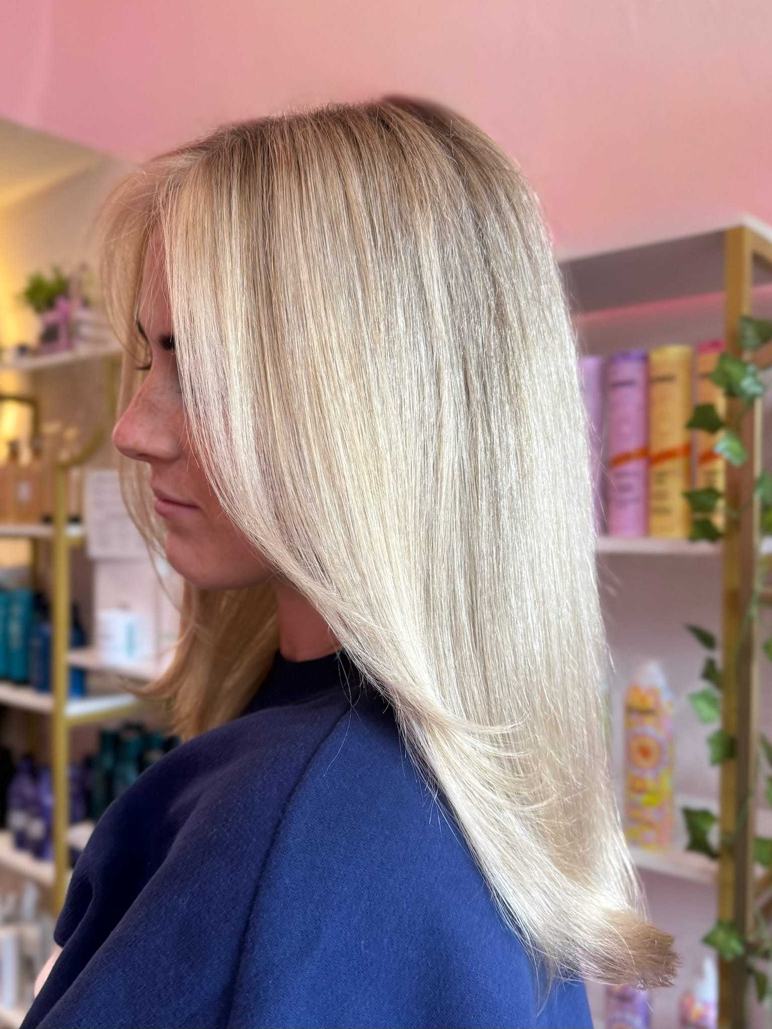 Blonde woman with straight hair in a salon, shelves with hair products in the background.