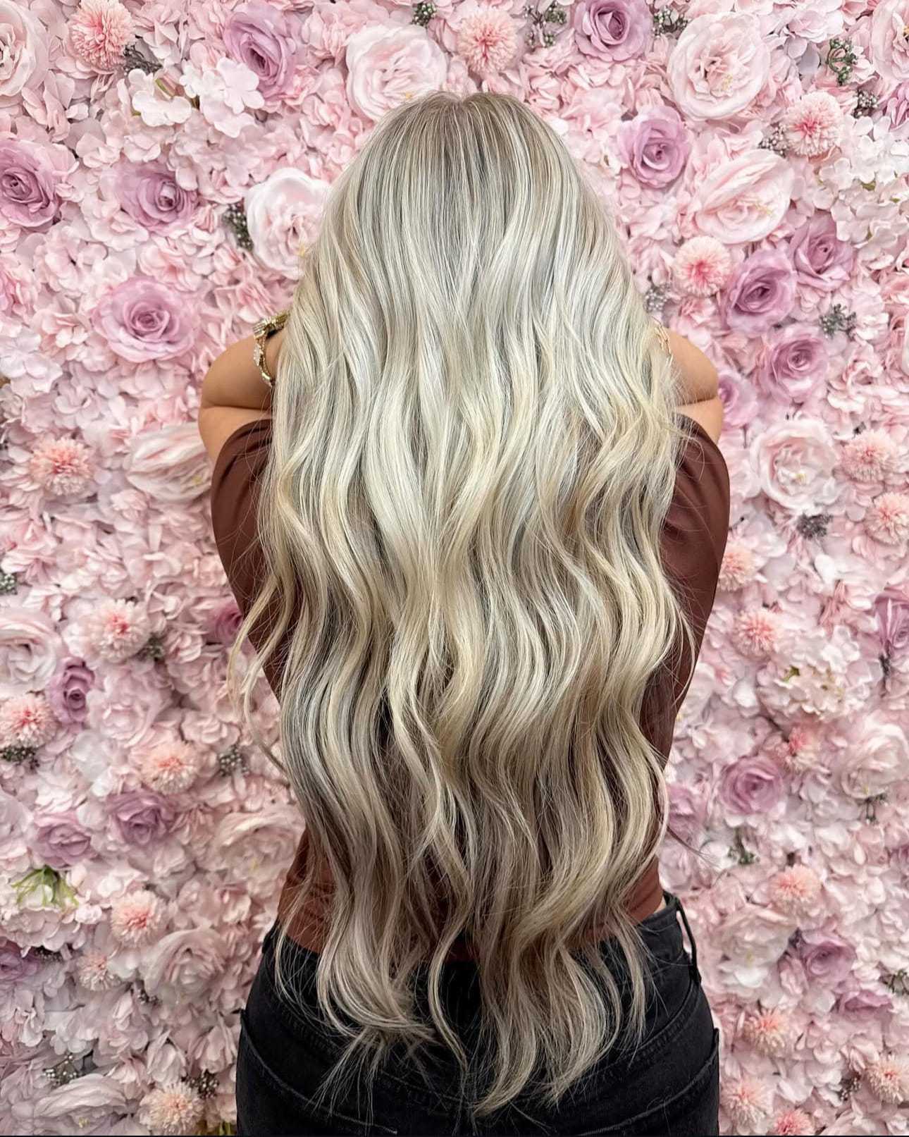 Long, wavy blonde hair against a pink flower wall backdrop.